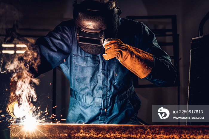 Metal welder working with arc welding machine to weld steel at factory while wearing safety equipmen