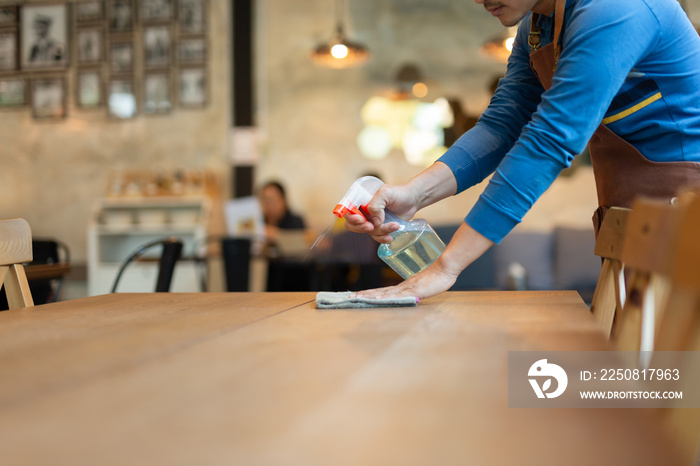 Waiter cleaning the table with spray disinfectant on table in restaurant.