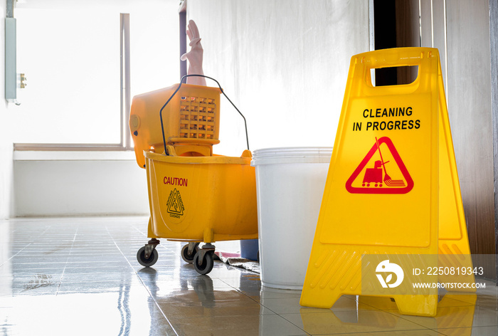 Close up yellow warning sign with message Cleaning in progress with cleaning trolley background