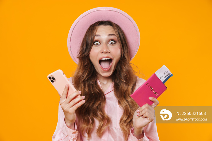 Image of excited woman in hat holding passport with ticket and mobile phone