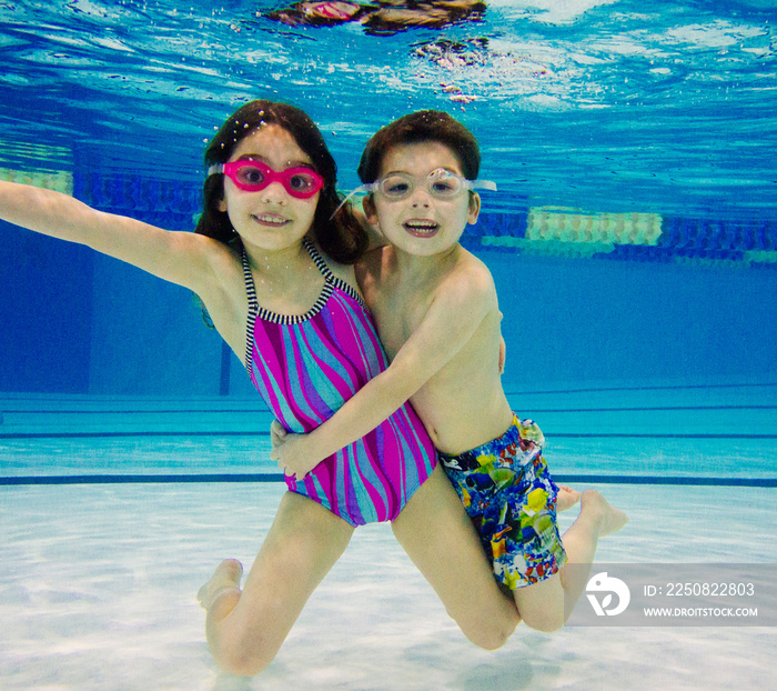 游泳池里水下的男孩和女孩戴着护目镜看着镜头微笑