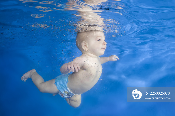 小男婴学会在水下游泳。婴儿在蓝色的水上游泳。