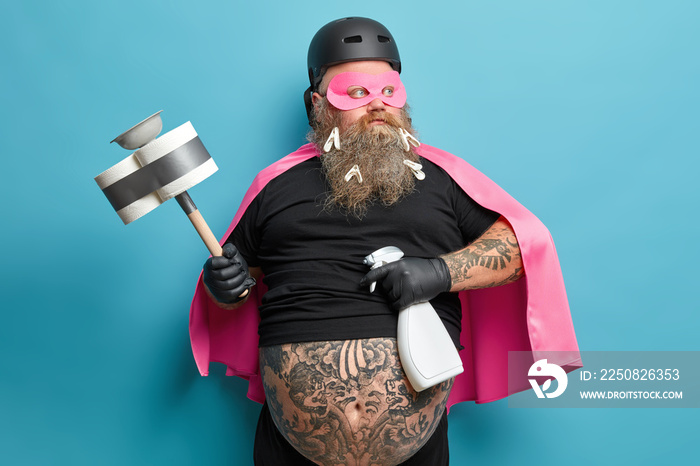 Serious confident man pretends to be superhero looks pensively aside poses with cleaning detergent a