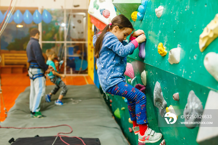 Little girl climbing a rock wall indoor