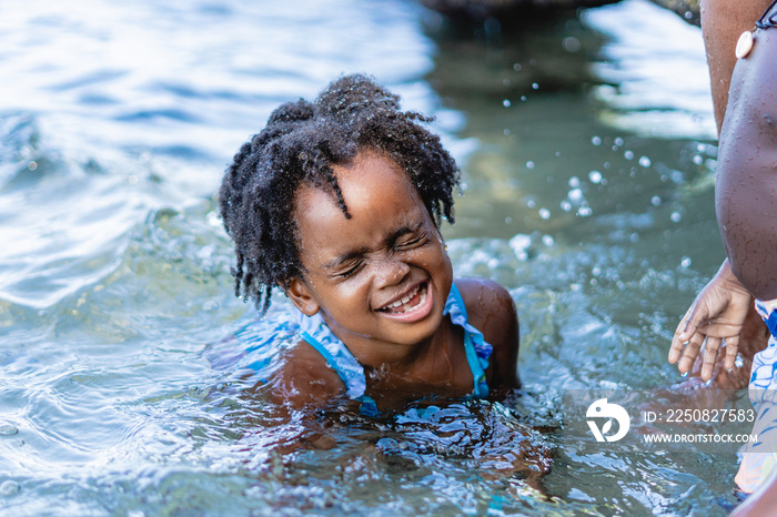 Imagen horizontal de una pequeña niña afroamericana de cabello afro en la playa en un día de verano 