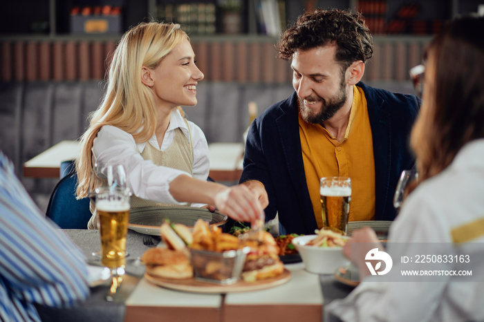 Multiethnic friends sitting at restaurant, drinking alcohol, chatting and having burgers for dinner.