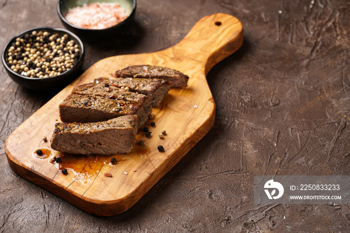一块木板上的熟牛肉牛排，切成片，白色和黑色，粗糙的海沙