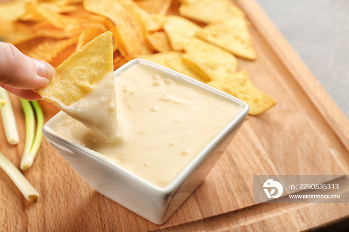 Female hand dipping nacho in bowl with beer cheese dip, closeup