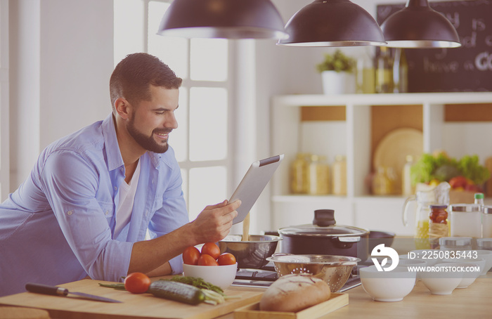 Man following recipe on digital tablet and cooking tasty and healthy food in kitchen at home