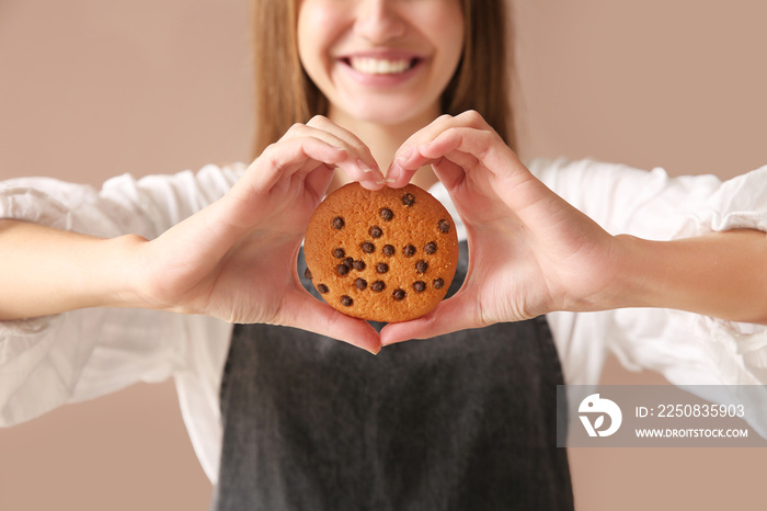 Beautiful female baker with tasty cookie on color background, closeup