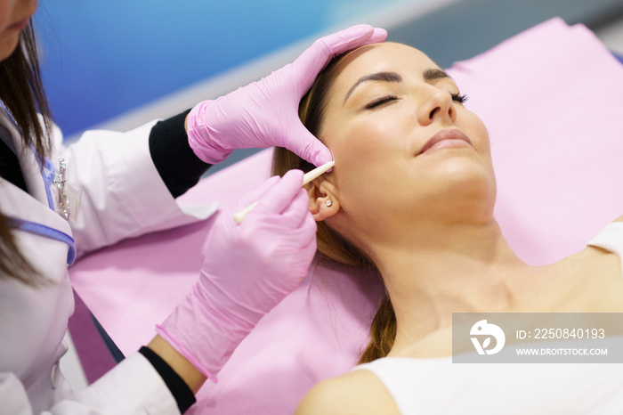 Doctor painting the area of a womans face where the PDO suture treatment threads will be injected.