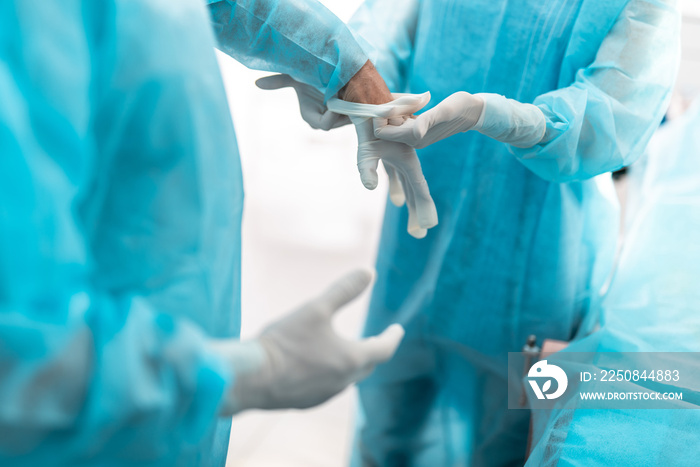 女性手臂在外科医生手上戴上白色无菌手套的特写。她们戴着蓝色手术手套