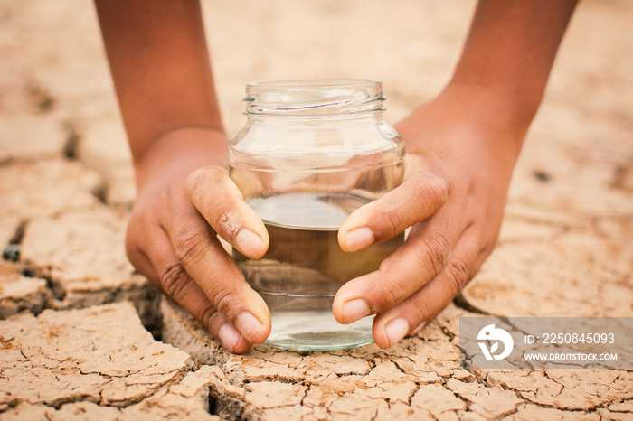 男孩的手拿着玻璃罐在开裂的干燥地面上，概念干旱和水危机