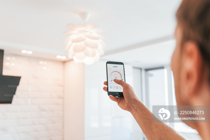 Rear view of adult man that is indoors controlling smart home technology