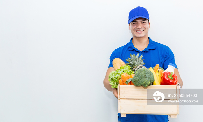 穿着蓝色制服的白人送货员的画像，手里拿着一篮子杂货新鲜蔬菜f