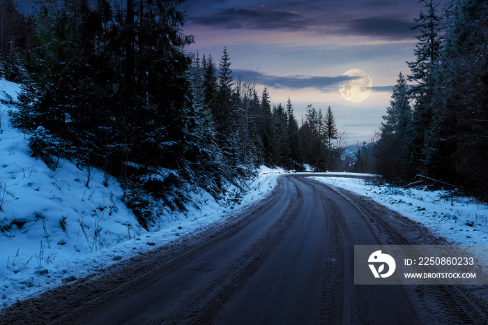 road through pine forest in mountains at night in full moon light. mysterious transportation winter 