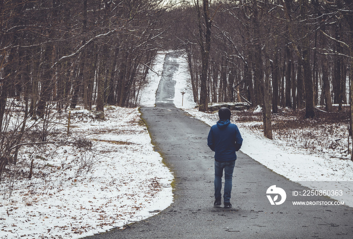 A man in blue jacket walks alone down road covered in debris surrounded by snow in winter, vintage s