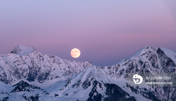 冬季满月在瑞士阿尔卑斯山升起，越过雷蒂孔山克洛斯特附近的山脉