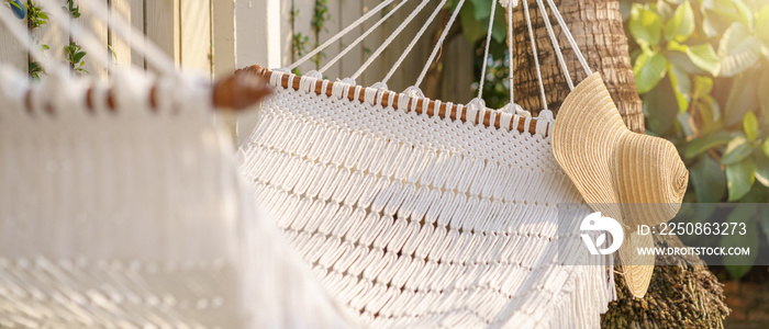 Straw hat hanging on white hammock outdoor. Relaxing summer vacation concept. Selective focus.