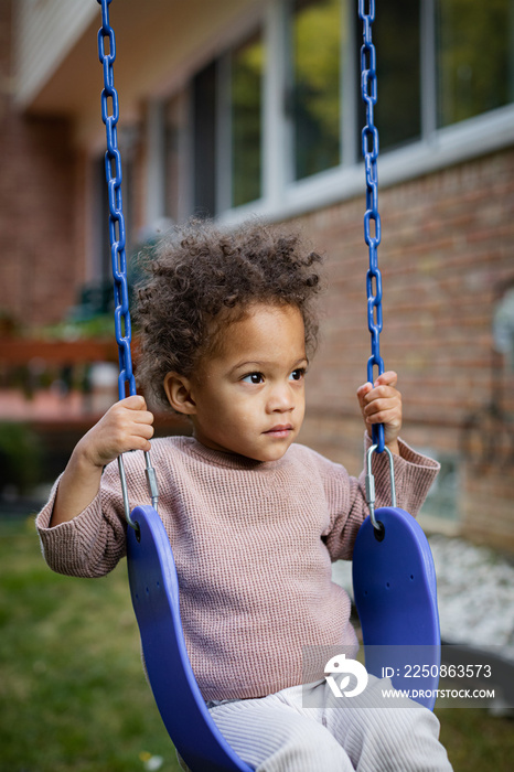 Biracial toddler plays on blue swings in backyard in fall