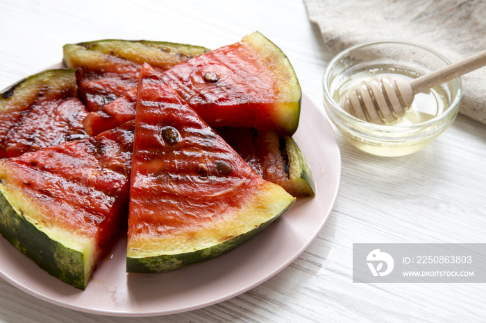 Slices of grilled watermelon with honey on a white wooden surface, side view.