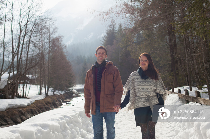 Portrait happy couple holding hands on sunny snowy footpath