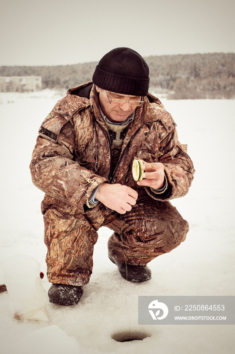 Senior man crouching while ice fishing in frozen lake