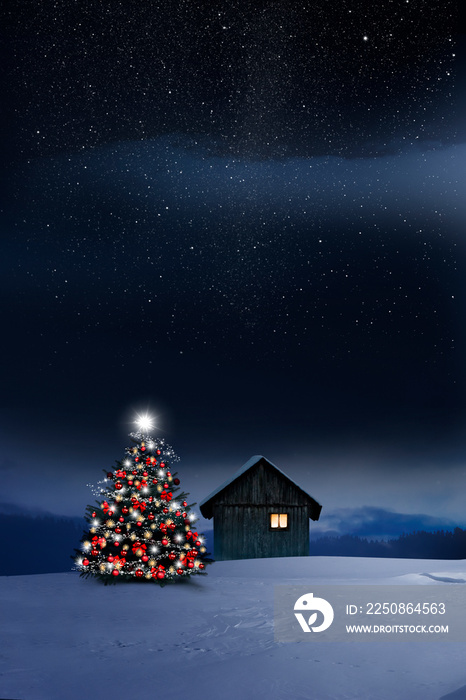 Glänzend leuchtender Christbaum im Schnee bei einer Holzhütte mit leuchtendem Fenster