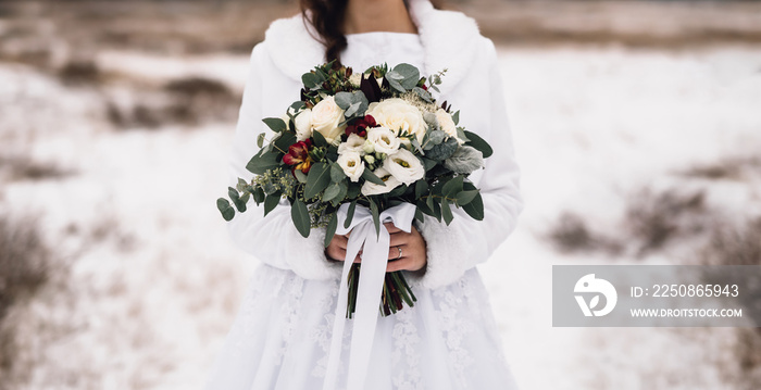 Bridal bouquet in hands of bride in white wedding dress with winter jacket. Wedding bouquet consisti