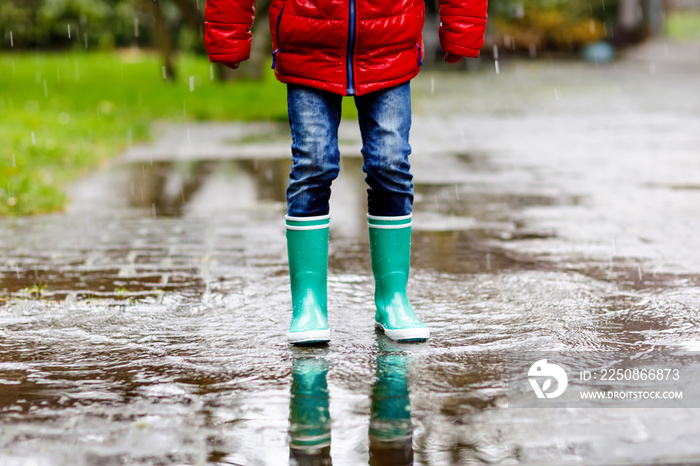 Close-up of kid wearing yellow rain boots and walking during sleet, rain and snow on cold day. Child