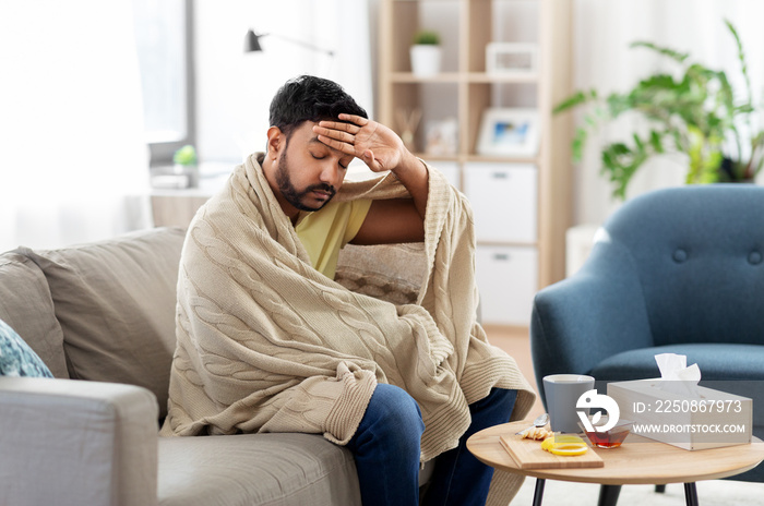 health, cold and people concept - sick young indian man in blanket having headache or fever with tea