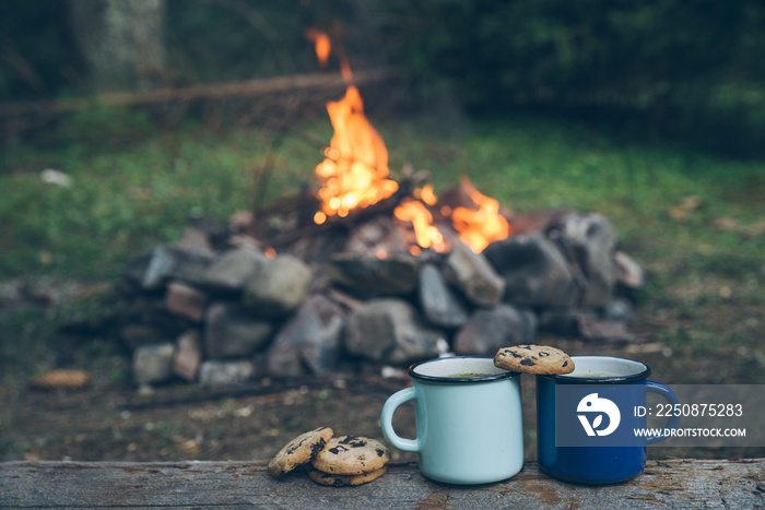 two metal cups with tea and cookies. fire on background