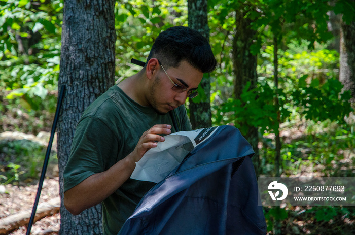 Young man setting up tent in forest