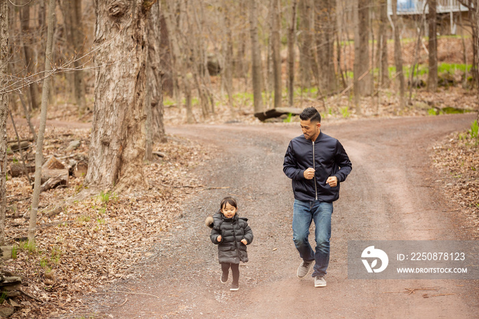 Father running with playful daughter on road against bare trees in forest