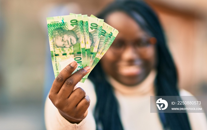 Young african american woman smiling happy holding south africa rands banknotes at the city.