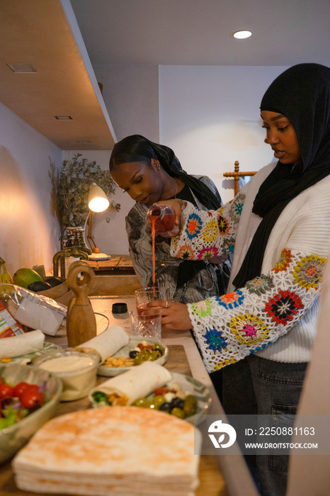 Woman wearing hijab pouring drink from bottle into glass in kitchen