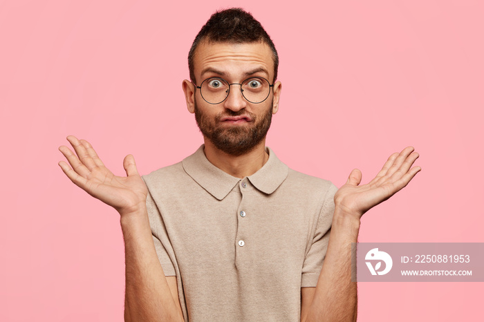 Doubtful handsome unshaven male student shrugs shoulders with uncertainty, being unsure doesn`t know