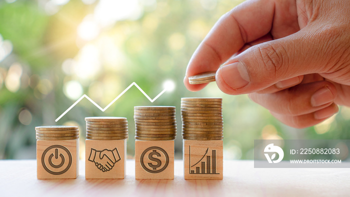 Hands that are stacking coins to save money And the symbols on the wooden blocks indicate business s