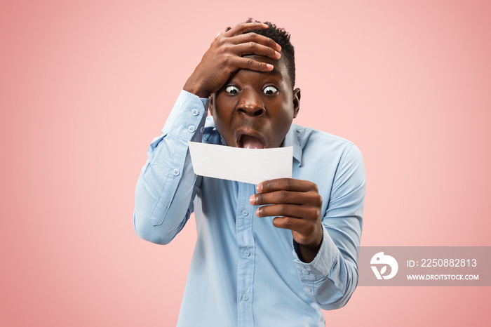 Young afro man with a surprised unhappy failure expression bet slip onpink studio background. Human 