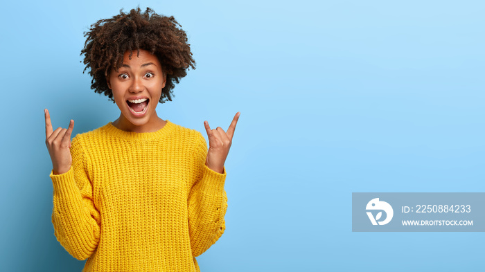 Excited lively energized curly woman makes heavy metal gesture, enjoys cool concert of favourite ban