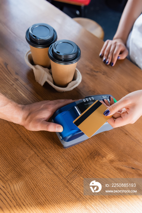 一个带着支付终端的咖啡师和一个在咖啡馆附近拿着信用卡去咖啡馆的女人