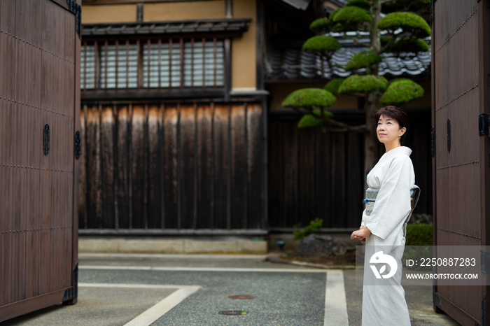 大きな屋敷の門前に立つ和服の女性