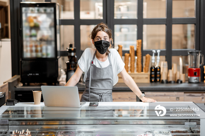 Portrait of a saleswoman or small business owner wearing medical mask at the counter in cafe or smal