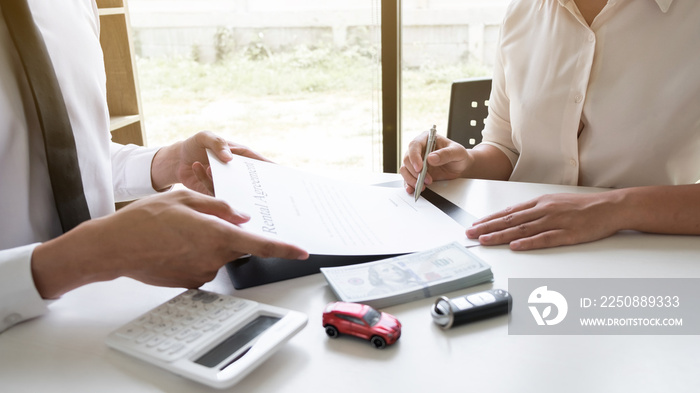 Customer is signing the car rental agreement and getting a car key from dealer after signed in the o