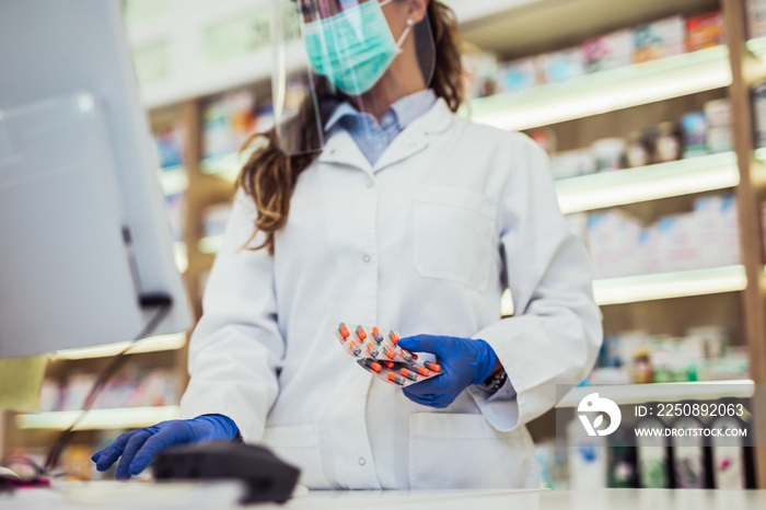 Female pharmacist with protective mask and face shield on her face ,working at pharmacy. Medical hea