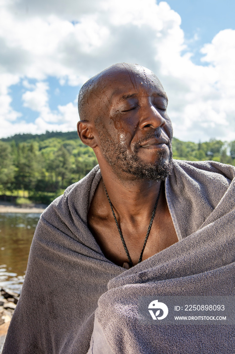 英国约克郡，一名男子裹着毛巾闭着眼睛坐在湖岸