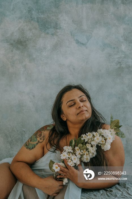 East Indian woman wrapped in blue fabric holding white flowers eyes closed