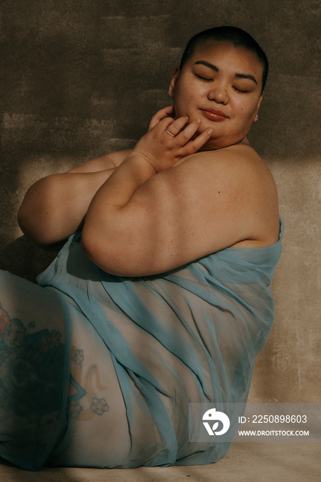 plus size filipino woman with shaved head wrapped in blue fabric sitting in the sun