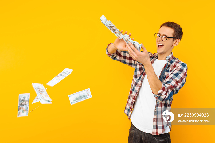 happy man, wearing glasses and a plaid shirt, throwing out money banknotes on a yellow background