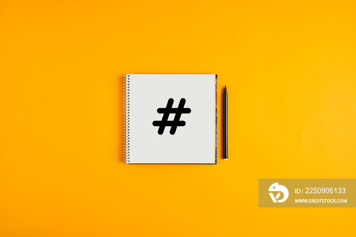 Hashtag icon drawn on a notepad with black pen next to it against yellow background